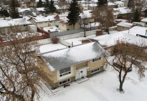 Snow-covered neighborhood with two-story houses and bare trees.