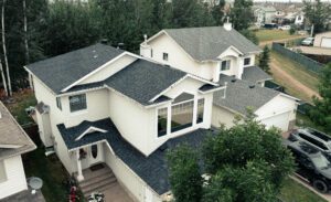 A house featuring a sloped roof and a paved driveway leading to the entrance, surrounded by greenery